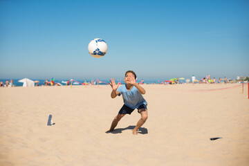 Concentrated preteen goalkeeper catching ball on beach. Boy playing soccer at seaside. Youth sport,...