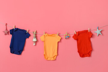 Different baby clothes and toys hanging on rope against pink background