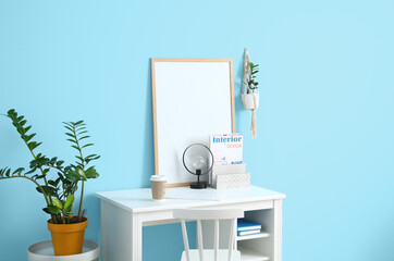 Stylish workplace with blank poster frame near color wall in modern room