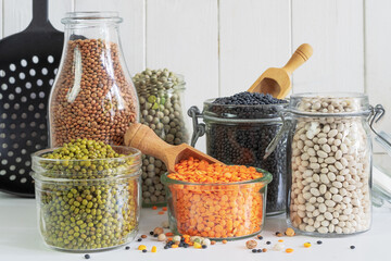 Assortment of colorful legumes in jars and glasses on a light kitchen table