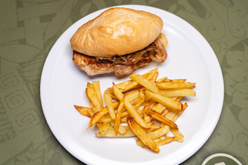 Aerial view of a plate with a pork and onion sandwich with fries