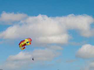Fototapeta na wymiar Young couple is flying in the blue sky using a colorful parachute. parasailing