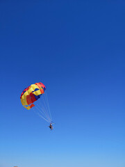 Fototapeta na wymiar Young couple is flying in the blue sky using a colorful parachute. parasailing