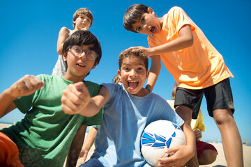 Portrait of excited preteen soccer players with ball looking at camera and shouting on beach....