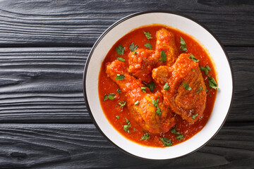 Ayam masak merah is a Malaysian dish made with chicken pieces that are doused in a rich, spicy, and creamy tomato sauce close-up in a bowl on the table. Horizontal top view from above