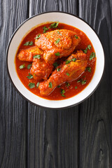 Ayam masak merah is a Malaysian traditional dish it is a casserole of chicken pieces in dried chillies sambal close-up in a bowl on the table. Vertical top view from above