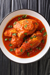 Ayam Masak Merah Delicious fried chicken marinated with turmeric and simmered in a mildly spiced tomato gravy close-up in a bowl on the table. Vertical top view from above
