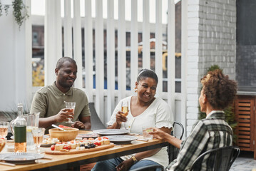 Portrait of modern African-American family enjoying drinks at dinner together outdoors