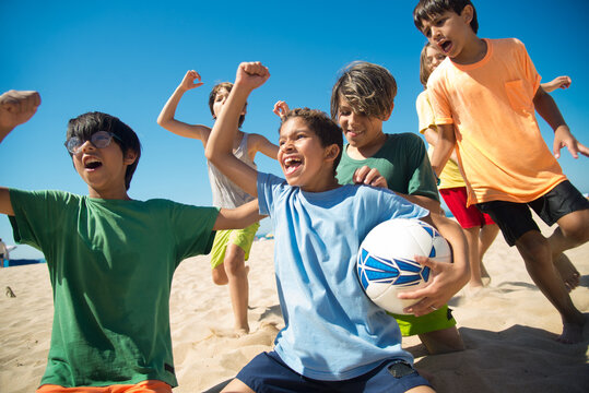 Excited preteen boys cheering after game on beach. Multiethnic friends playing football at seaside. Summer vacation and friendship concept