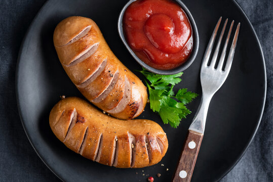 Grilled sausages and ketchup on black plate, top view