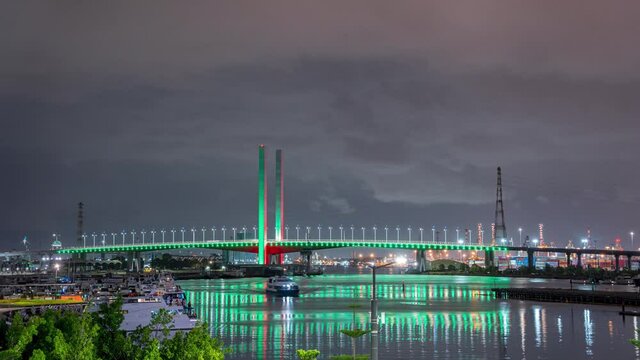 Night time lapse of Melbourne iconic Bolte bridge with shimmering red and green Christmas light projections and party boats cruising pass, located in Docklands waterfront harbour, Victoria, Australia.