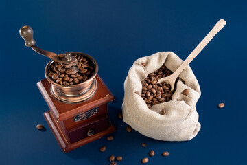 Grains of coffee in a manual coffee grinder on a dark blue background. Coffee in a canvas bag....