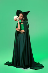 Young witch with skull on color background