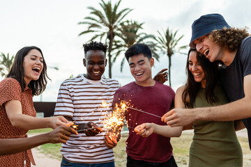 Happy multiracial people laughing and having fun together with sparkles outdoors - Young friends...