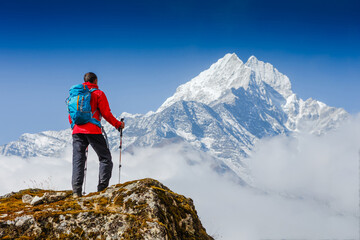 Hiker with trekking poles stands on the slope against the background of high snow-capped mountains