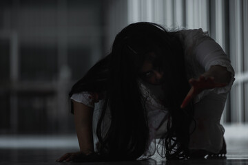 Naklejka premium Horror evil woman ghost creepy crawling move slowly creeping out in a dark room at house. Female zombie in blood devil is scary she haunted at the abandoned building, Happy Halloween festival concept