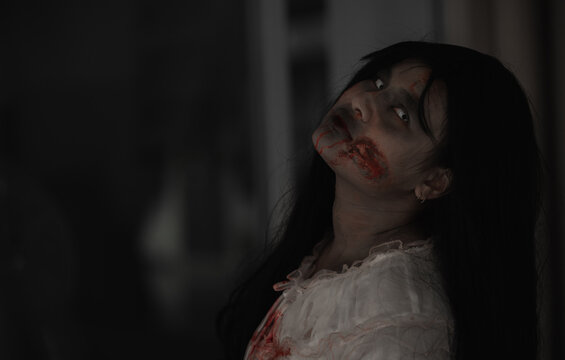 Female zombie in blood. Closeup face and eyes of Asian Woman ghost with blood. Horror creepy scary fear in a dark house. Hair covering the face, Halloween festival concept