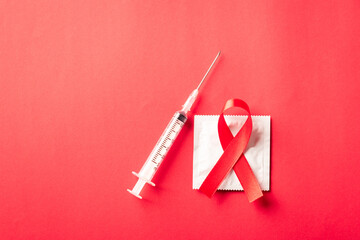 Red bow ribbon symbol HIV, AIDS cancer awareness, condom and syringe with shadows, studio shot isolated on red background, Healthcare medicine sexually concept, World AIDS Day