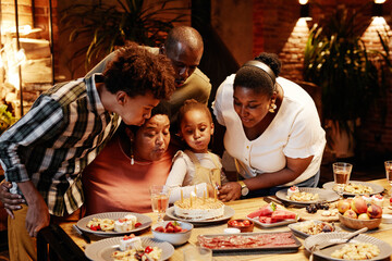 Portrait of African- American grandma blowing candles while celebrating Birthday with family in cozy setting
