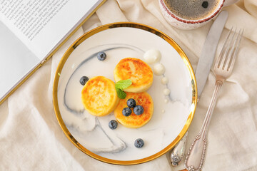 Plate with cottage cheese pancakes and blueberries on light fabric background
