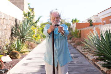 Front view of attractive smiling senior man in outdoors looking at camera holding a walking cane