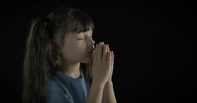 Praying child. Cute little girl prays on a black background. Child and religion.