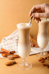 Woman putting straw in glass with tasty almond latte on color background