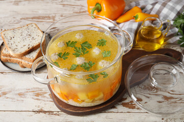 Pot with tasty meatball soup and bread on light wooden background