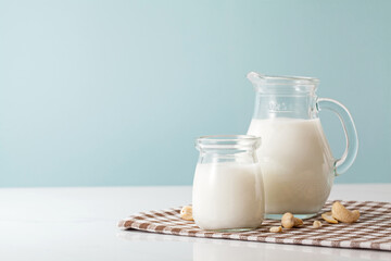 A bottle and pot of milk with nuts on cyan background.