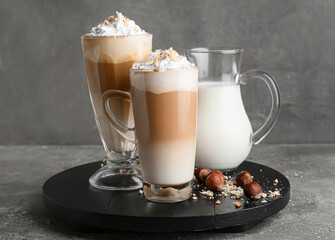 Glass and cup of tasty latte with nuts on grunge background