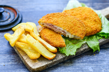 
 Crispy  deep fried home made     chicken Cordon bleu with cheese   and ham  and french fries on wooden rustic background.  
