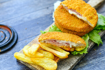 
 Crispy  deep fried home made     chicken Cordon bleu with cheese   and ham  and french fries on wooden rustic background.  