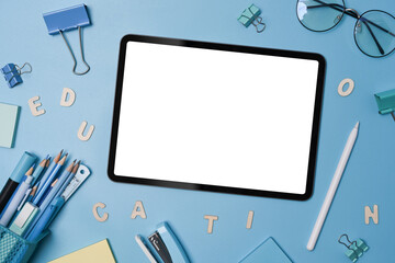 Mock up digital tablet with white screen, stylus pen and various stationery on blue background.
