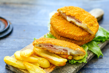 
 Crispy  deep fried home made     chicken Cordon bleu with cheese   and ham  and french fries on wooden rustic background.  