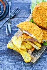 
 Crispy  deep fried home made     chicken Cordon bleu with cheese   and ham  and french fries on wooden rustic background.  