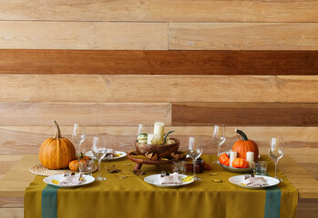 Beautiful table setting with fresh pumpkins and fallen leaves near wooden wall