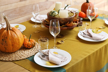 Beautiful table setting with fresh pumpkins and fallen leaves near wooden wall