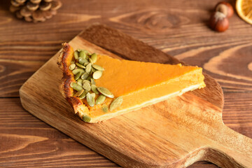 Board with piece of delicious pumpkin pie on wooden background