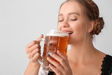 Beautiful woman drinking beer from mug on light background