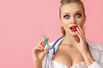 Shocked sexy young woman dressed as doctor with syringe on color background