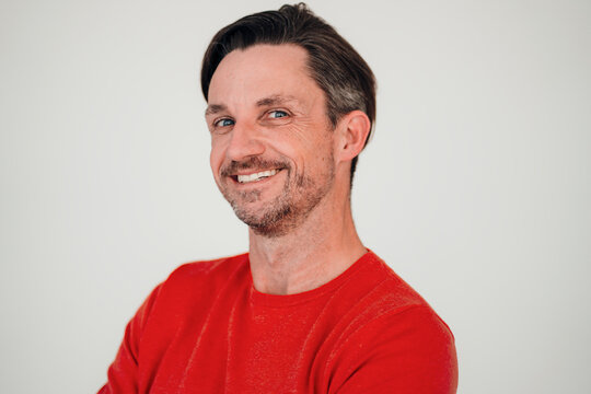 Smiling mature man with hair stubble in front of white wall