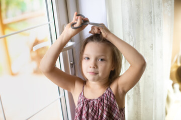 Cute funny caucasian girl child with scissors cuts her hair, hooliganism and pranks child, child with a funny oblique haircut - obrazy, fototapety, plakaty