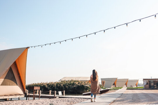 A girl in a plaid with long hair walks along the river bank. Morning on vacation at the glamping.