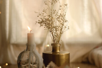 Candle holders with lit candles, vase with gypsophila flowers and bokeh lights. Hygge at home. Selective focus.