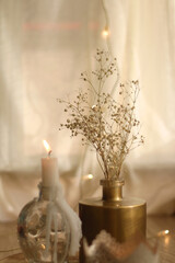 Candle holders with lit candles, vase with gypsophila flowers and bokeh lights. Hygge at home. Selective focus.