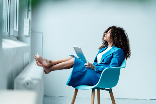 Mature businesswoman with laptop looking up while sitting on chair