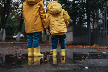 Children in yellow rubber boots and autumn jackets are jumping in a puddle. Autumn mood.