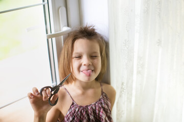 Happy caucasian girl child with scissors cuts off her hair, hooliganism and mischief child, child with a funny oblique haircut, child cut his hair - obrazy, fototapety, plakaty