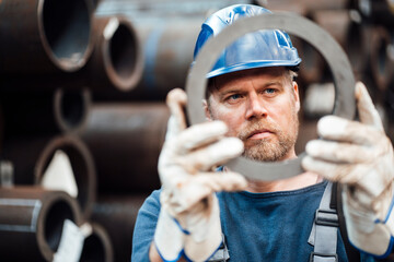 Male inspector checking circle shape steel equipment in warehouse