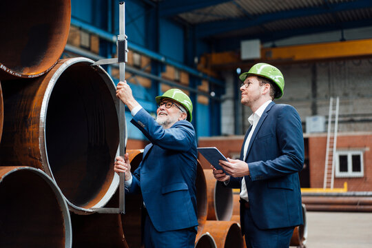 Male professional measuring pipe with caliper while standing by coworker at warehouse